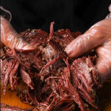 Hands pulling apart tender, seasoned, and juicy shredded beef on a wooden board.