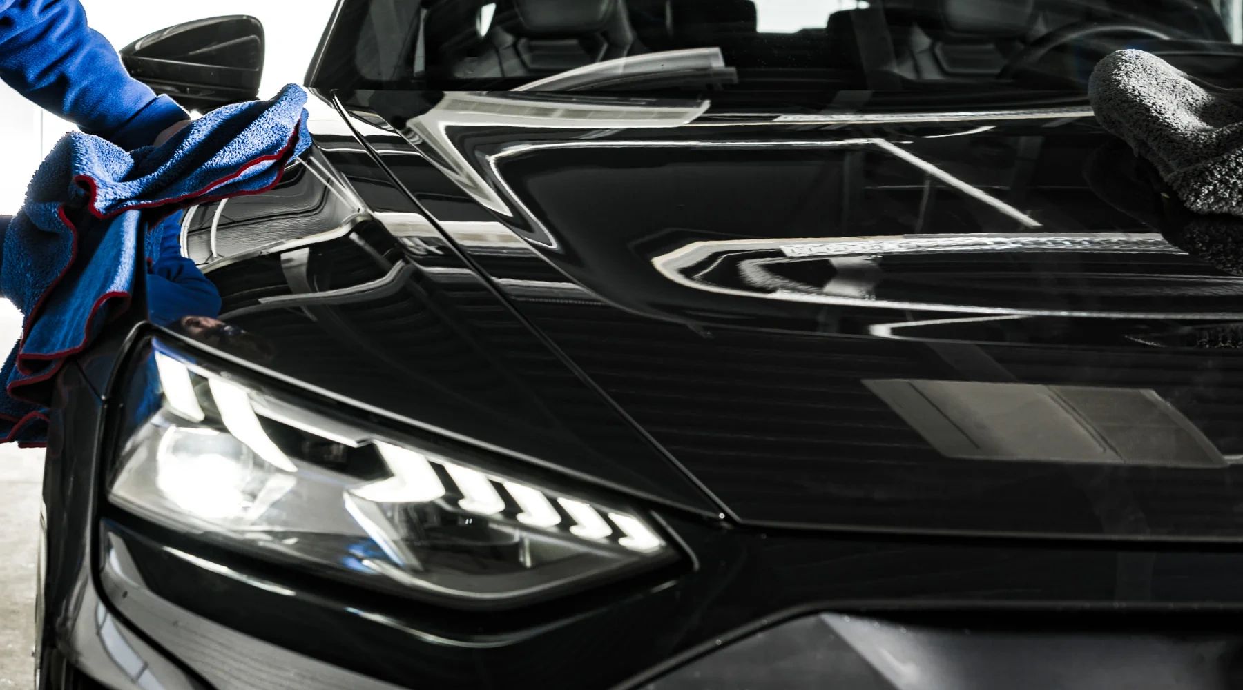 Person polishing a black car's hood with a blue cloth.