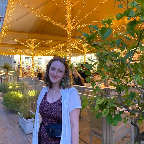 Young woman smiling outdoors with decorative lights.