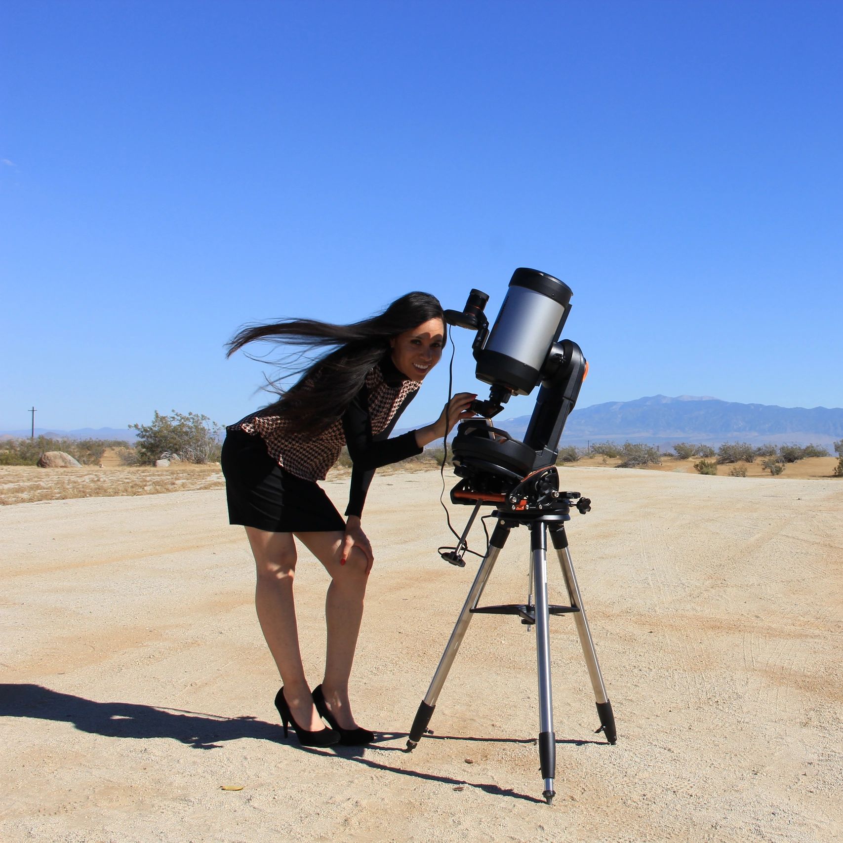 Woman observing the sky with a telescope in a desert landscape.