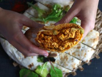 Two hands holding a full Paneer Tikka Wrap