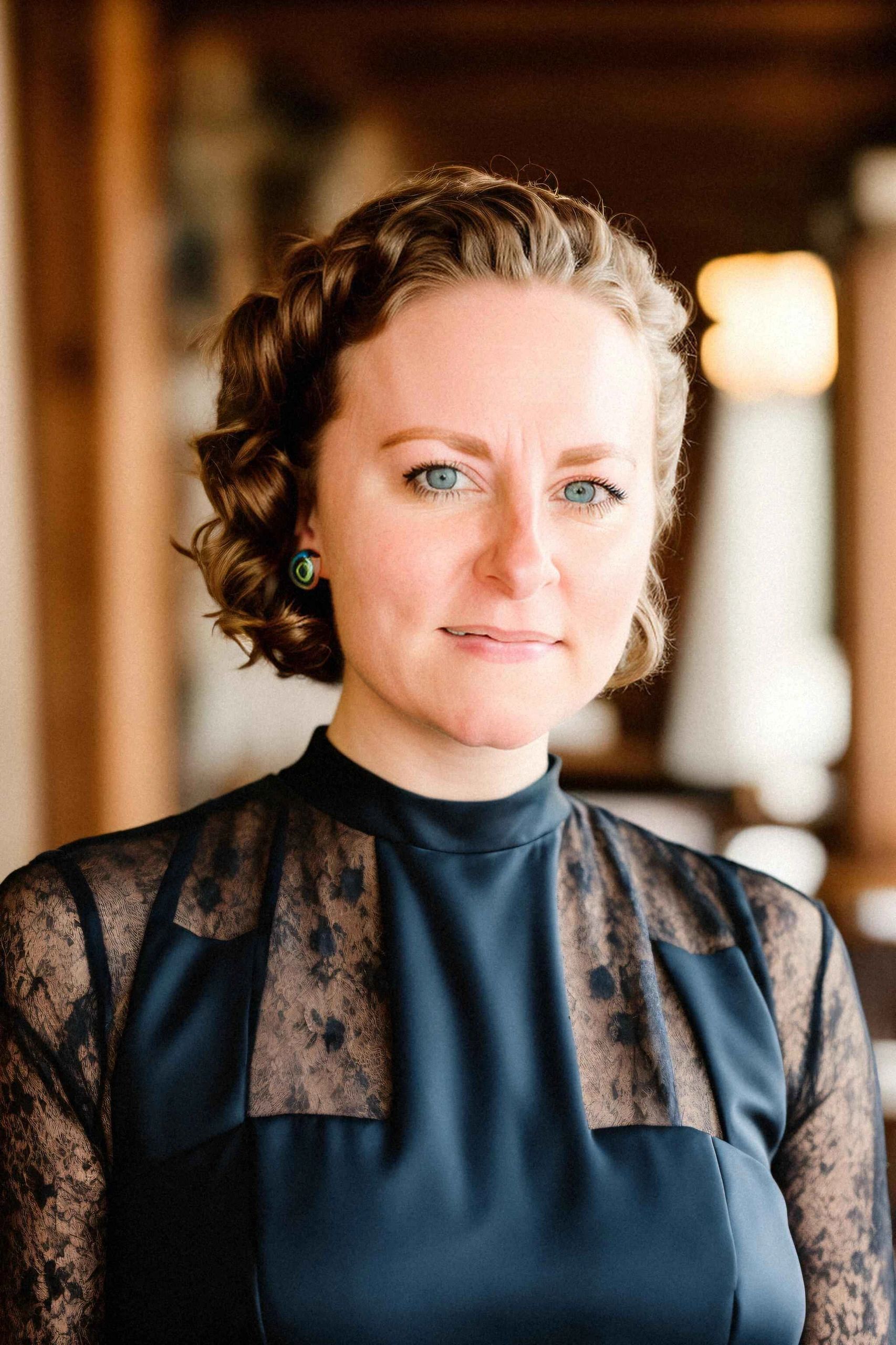 Woman in black lace blouse smiling with blurred office space in the background.