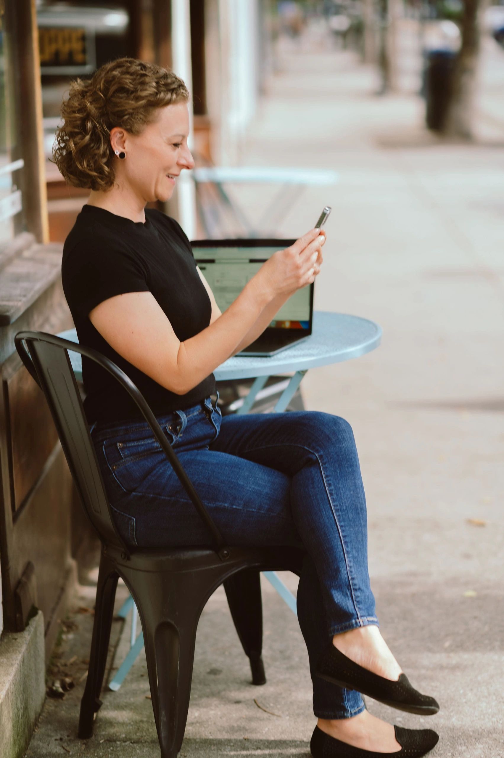 Rayni Collins, online sleep therapist, working remotely with phone and laptop at a café table