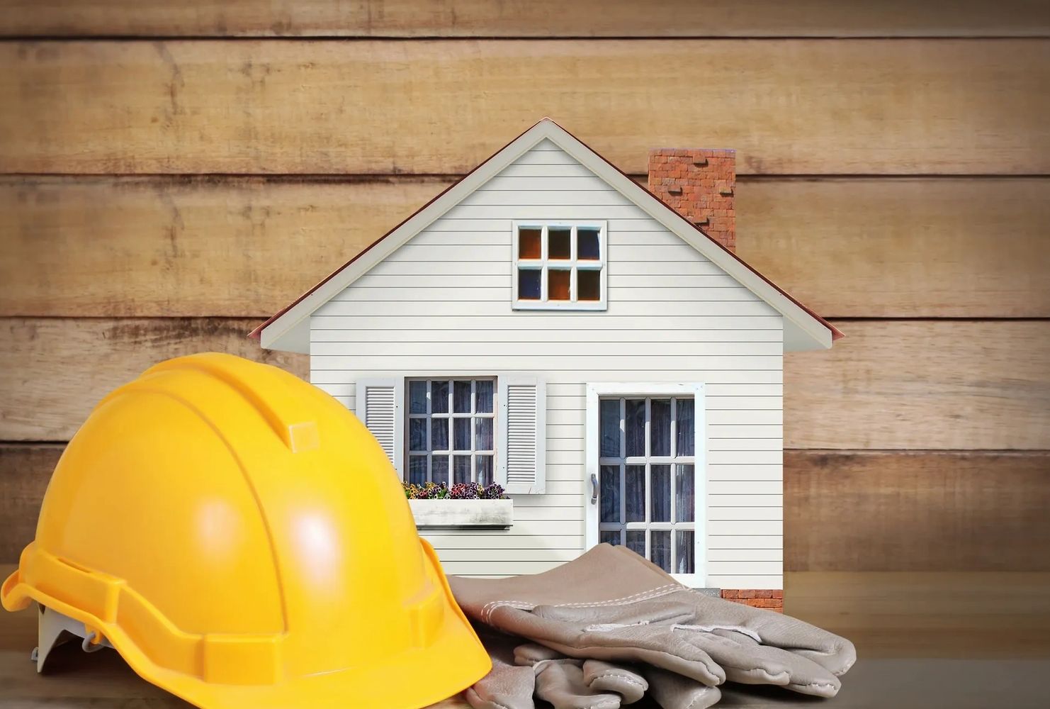 Yellow construction helmet and gloves with a miniature house model.