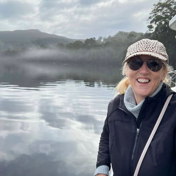 Smiling woman in sunglasses and cap near misty lake and forest.