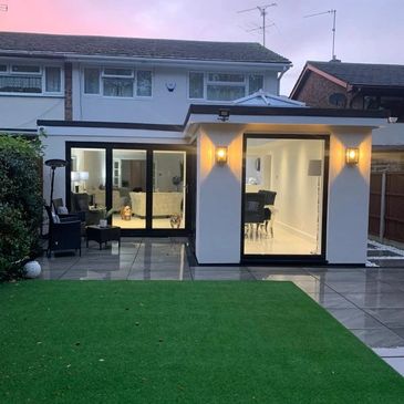 Modern house extension with large glass doors and a well-lit interior at dusk.