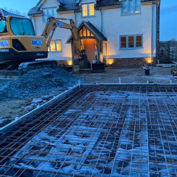 Excavator working on driveway construction in front of a house at dusk.