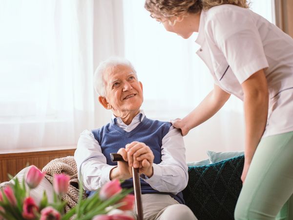 Senior with a walking stick being comforted by the nurse in the hospice.