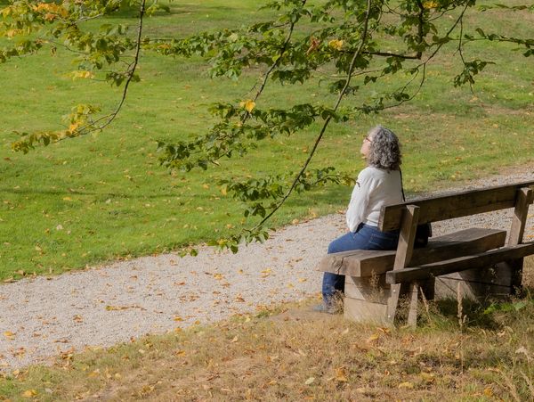 Mature Mexican woman with gray-black hair sitting on a wooden bench sunbathing on a sunny summer day