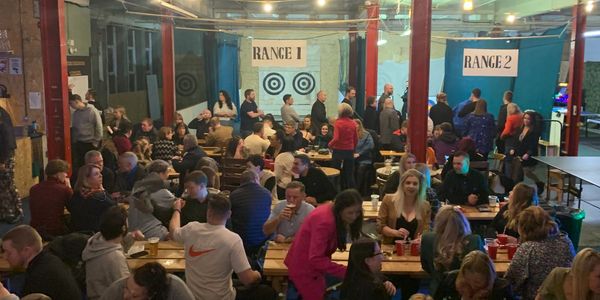 Group of people drinking with axe throwing and archery in the background