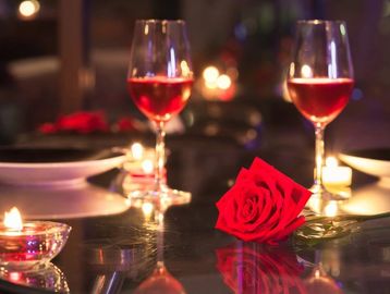 Dinner table for two with wine glasses and a red rose centerpiece.