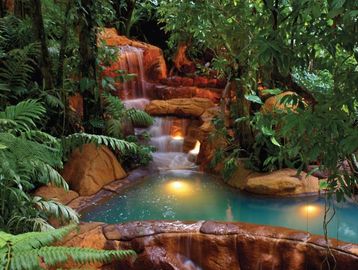 Peaceful mineral hot spring with a waterfall in the background.