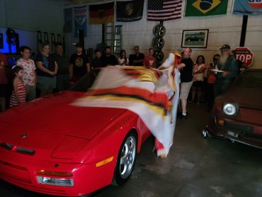man pulling off the Porsche flags to revel a 1986 red Porsche 944 Turbo