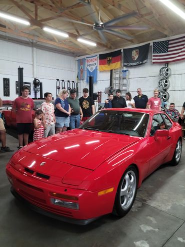 People standing around and admiring the Red 1986 Porsche 944 Turbo