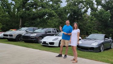 Husband and wife standing in front of several different models of Porsche