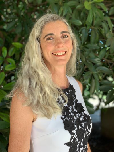 Professional woman with wavy long silver hair in a sleeveless dress with a smile, Heather Ball, MBA