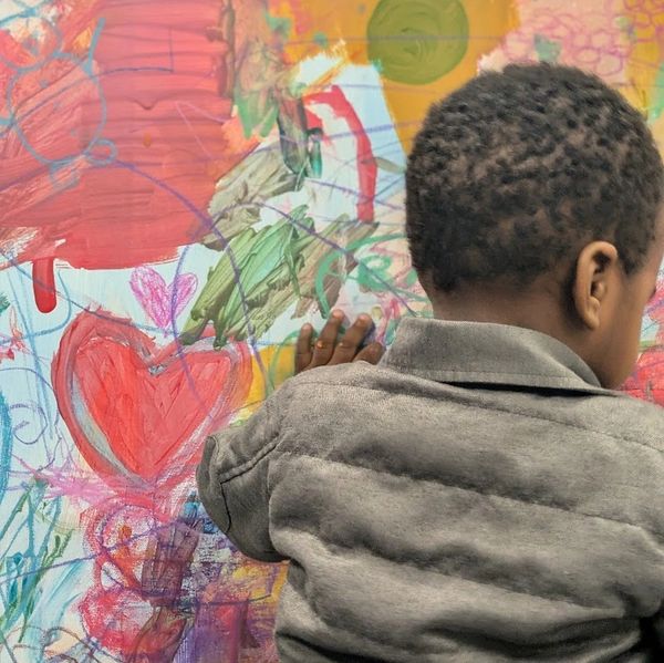 Child drawing colorful hearts and shapes on a wall.