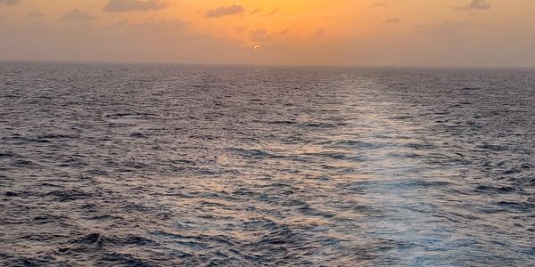 Sunset over a vast ocean with gentle waves and golden sky.