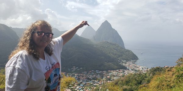 A woman points at twin peaks overlooking a coastal town under a cloudy sky.