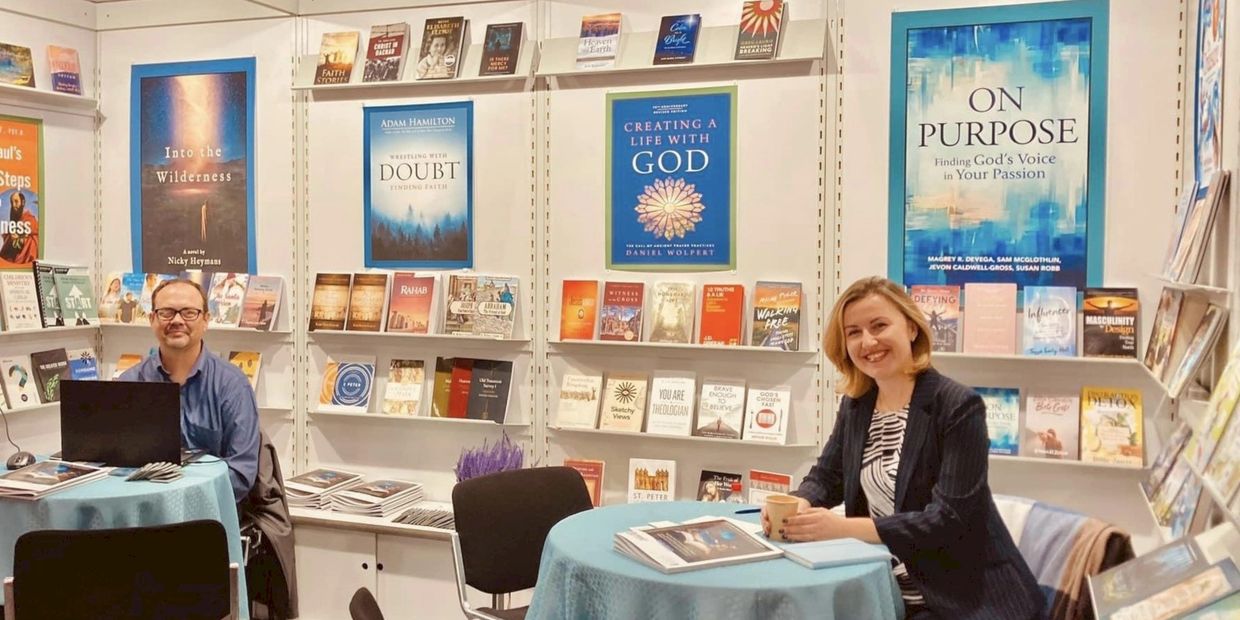 Two people at a book fair booth with Christian-themed books on display.