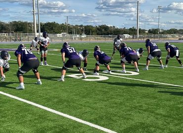 Football teams lined up at the line of scrimmage on a sunny field.