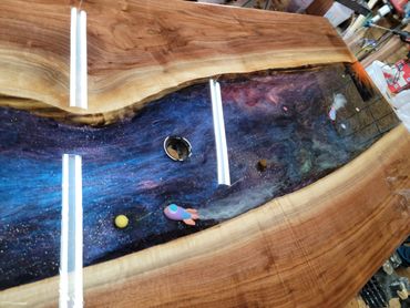 A wooden table with a galaxy-themed epoxy resin river and small rocket models.