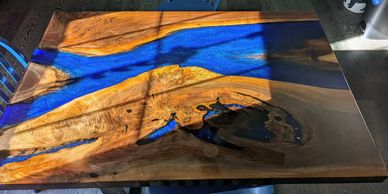 Wooden table with blue resin river design in natural light.