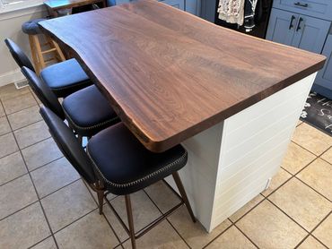 Smooth wooden countertop with black cushioned bar stools in a kitchen.