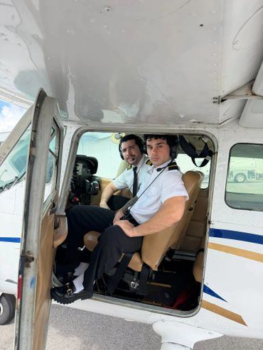 Two pilots seated inside a small airplane cockpit, wearing headsets and uniforms.