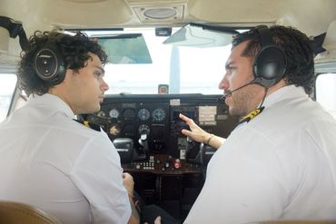 Two pilots in uniform with headsets inside a small aircraft cockpit.