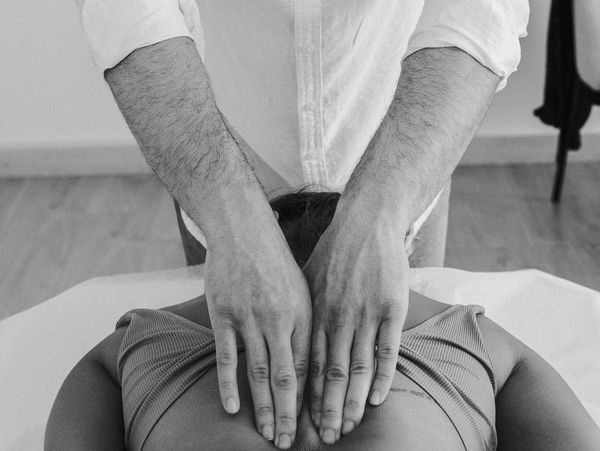 Person receiving a back massage from a therapist wearing a white shirt.
