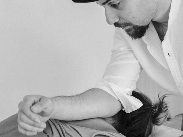 A man in a white shirt providing physical therapy or massage to another person.