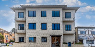 Modern three-story apartment building with white brick exterior and blue windows under a blue sky.