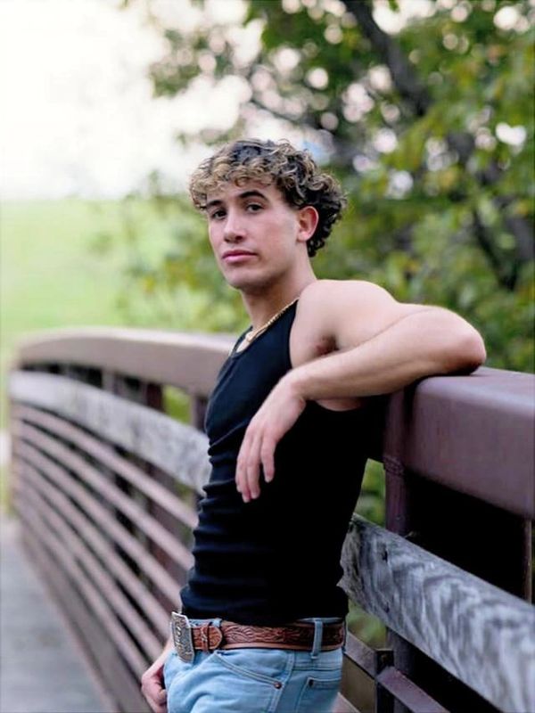 Young man leaning on a bridge railing outdoors.