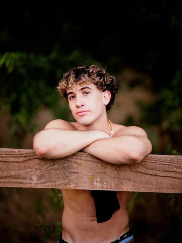 Young man leaning on wooden fence outdoors.