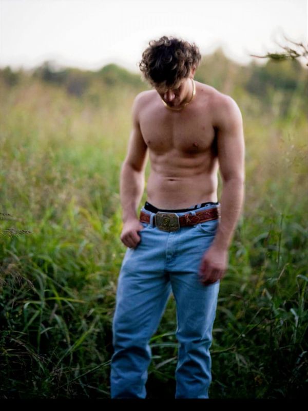 Shirtless man standing in a grassy field.