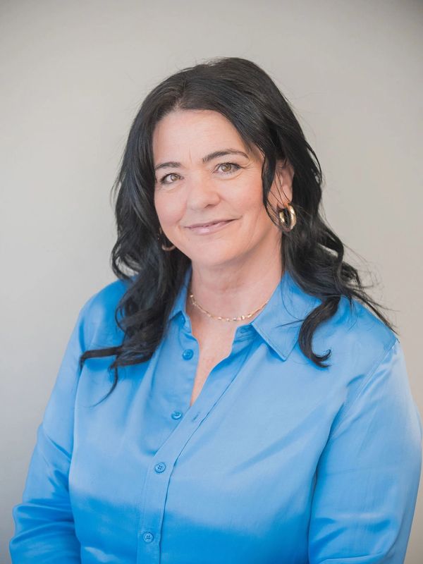 Smiling woman with black hair wearing a blue shirt and gold hoop earrings.