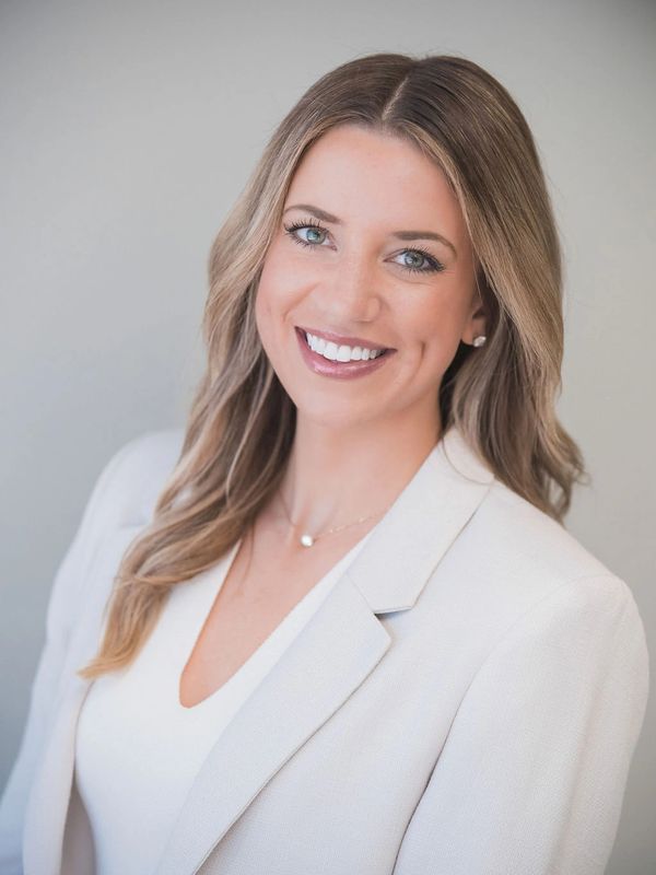 Smiling woman with long hair in a light beige blazer and white top.