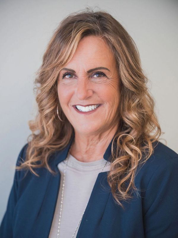 Smiling woman with curly hair wearing a navy blazer and light top.