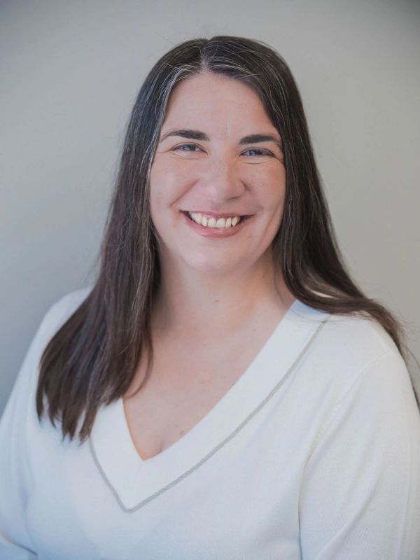 Smiling woman with long dark hair wearing a white V-neck sweater.