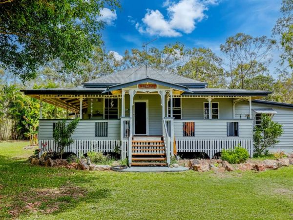 Charming country house with a wraparound porch and lush greenery under a bright blue sky.