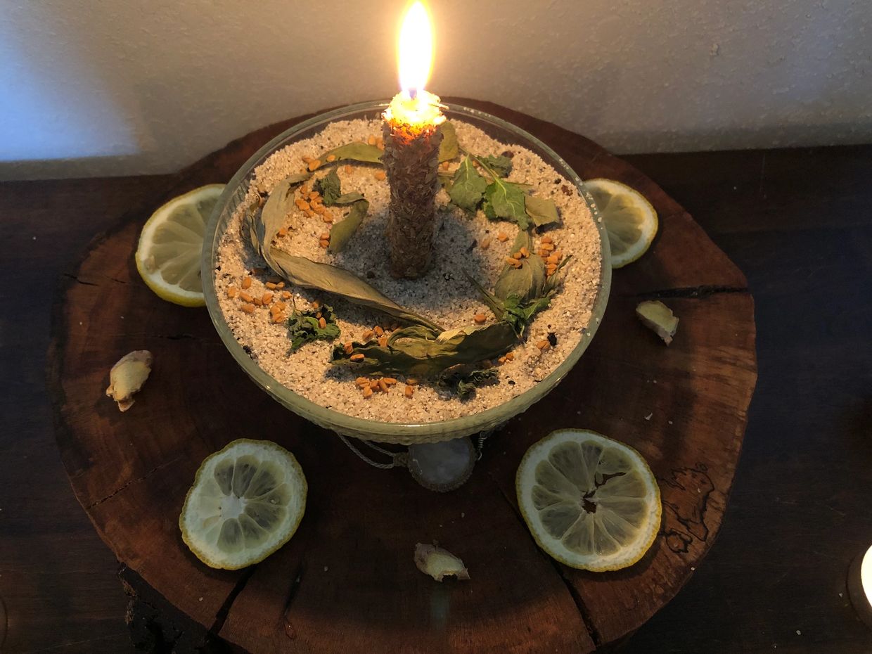 Lit herbal candle on sand with lemon slices.