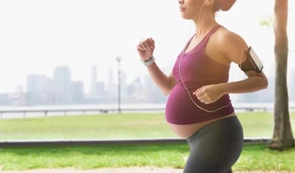 Pregnant woman jogging outdoors with earphones.