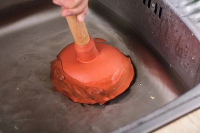 A person using a plunger in a sink filled with water.