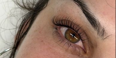 Close-up of a brown eye with long eyelashes and well-defined eyebrows.