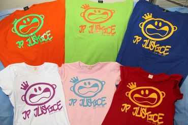 A colorful variety of JP JUSTICE logo T-shirts laid out flat in bright orange, green, blue, pink, an