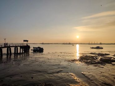 Sunset over a calm waterfront with boats and a pier.