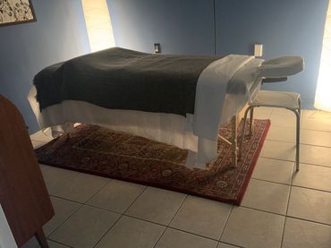 Massage table in a softly lit room with warm lamps and a decorative rug.