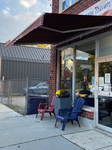 Two chairs and a flower pot outside a brick building with an awning.