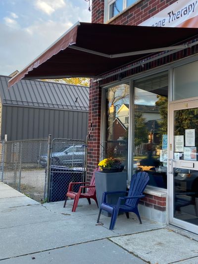 Outdoor seating with chairs and a flower pot under a brown awning by a brick building.
